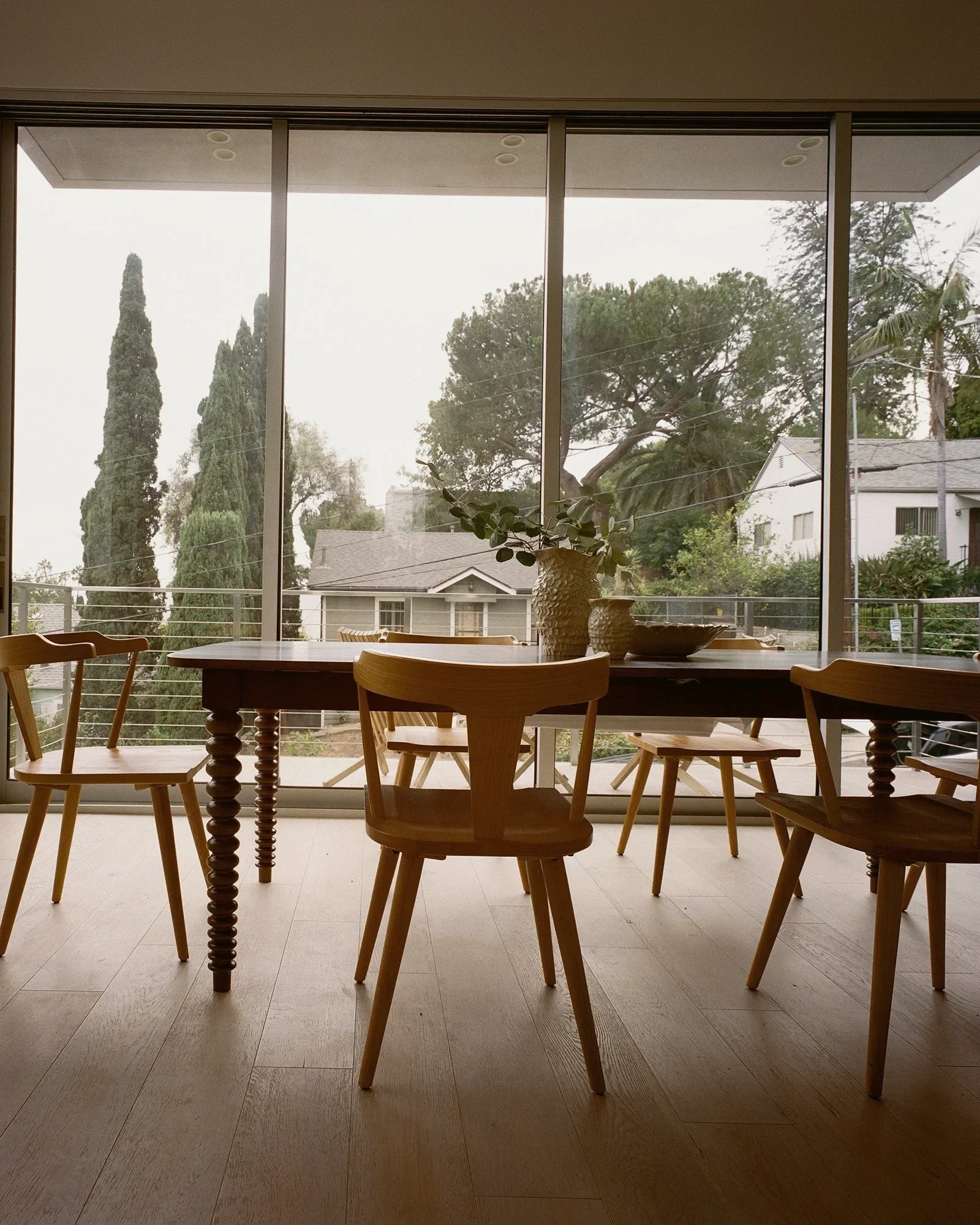 Silver Lake dining room with spindle back chairs and a dark wood table set against a full-height window wall of cypress trees, staged by Nesting Dolls Design