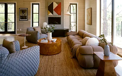Laurel Canyon living room with quilted blue-gray armchairs, a modular sofa and a geometric canvas above a concrete fireplace, staged by Nesting Dolls Design