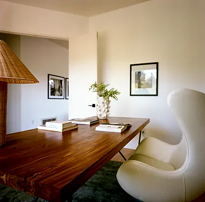 Laurel Canyon home office with a solid teak desk, a white leather Egg chair, a woven rattan table lamp and framed photographs, staged by Nesting Dolls Design