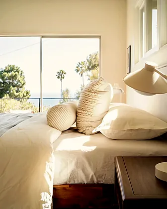 Rancho Palos Verdes bedroom in white linen with textured bolsters and open ocean through the window, staged by Nesting Dolls Design
