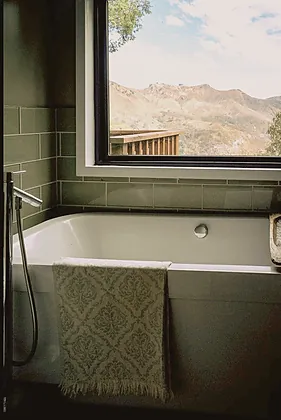 Topanga Canyon bathroom with green glazed tile, a soaking tub and a patterned bath sheet, with the canyon ridge through the window, staged by Nesting Dolls Design