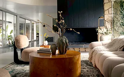 View Park living room with a black board-and-batten chimney breast, original stonework and a round burl coffee table, staged by Nesting Dolls Design