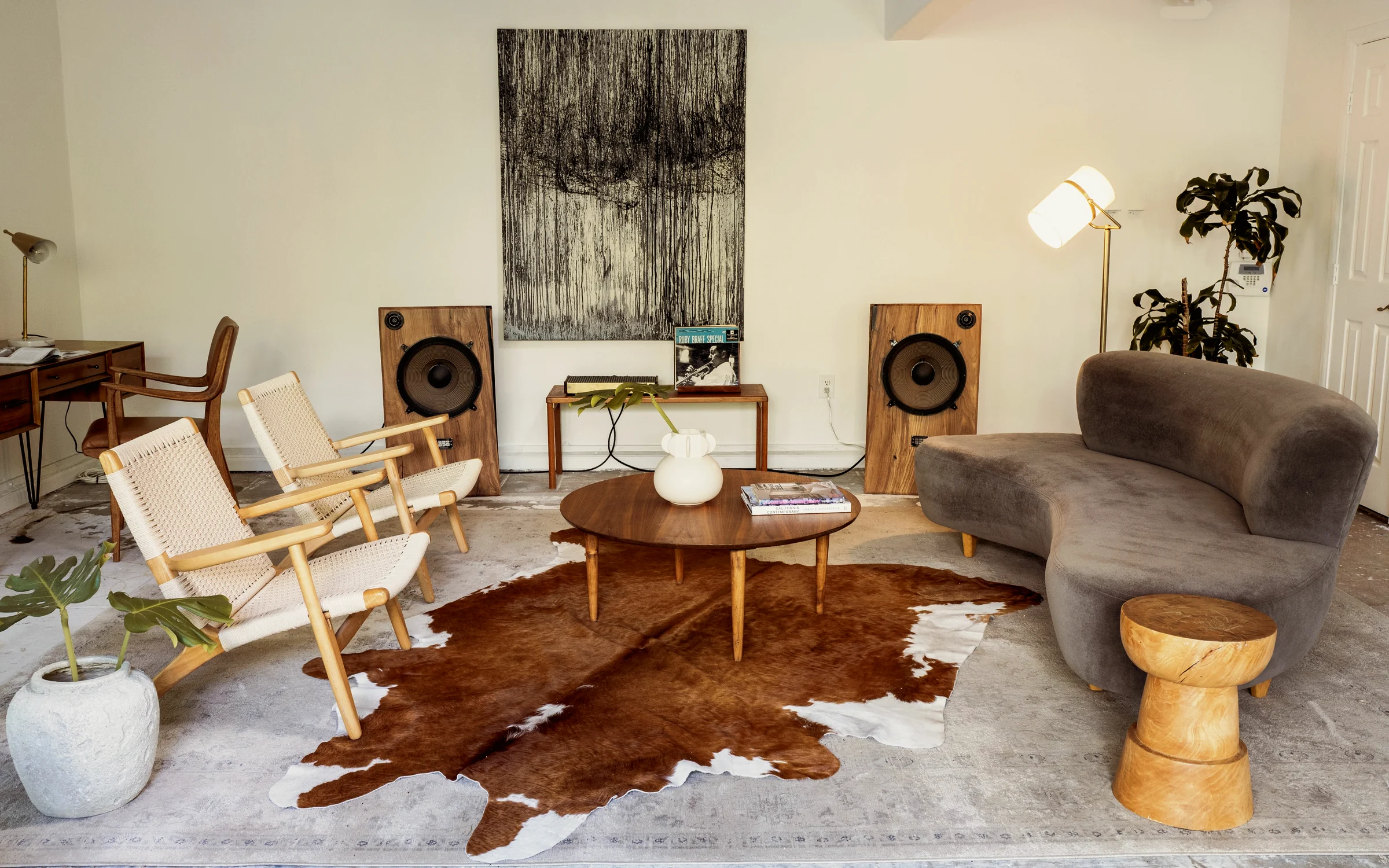 Larchmont ADU listening room with open-baffle loudspeakers in solid walnut cabinets either side of a console table, paper-cord lounge chairs and a curved grey sofa on a cowhide rug, staged by Nesting Dolls Design