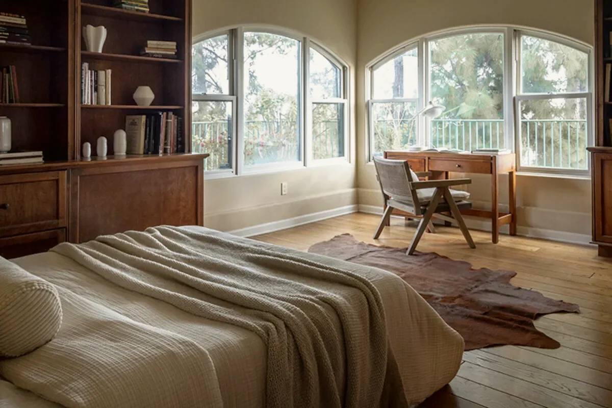 Beverly Hills bedroom with a writing desk beneath arched windows, a linen headboard and layered textured bedding, staged by Nesting Dolls Design