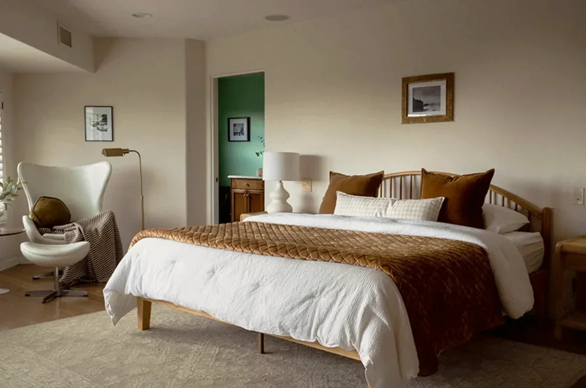 Beverly Hills master suite with a white leather Egg chair in the corner, a low bench and warm neutral bedding, staged by Nesting Dolls Design