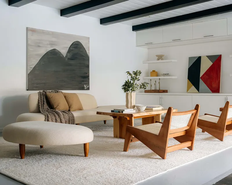 Living room of a preserved 1958 midcentury house in View Park, Los Angeles, with exposed dark ceiling beams and cane lounge chairs, staged by Nesting Dolls Design