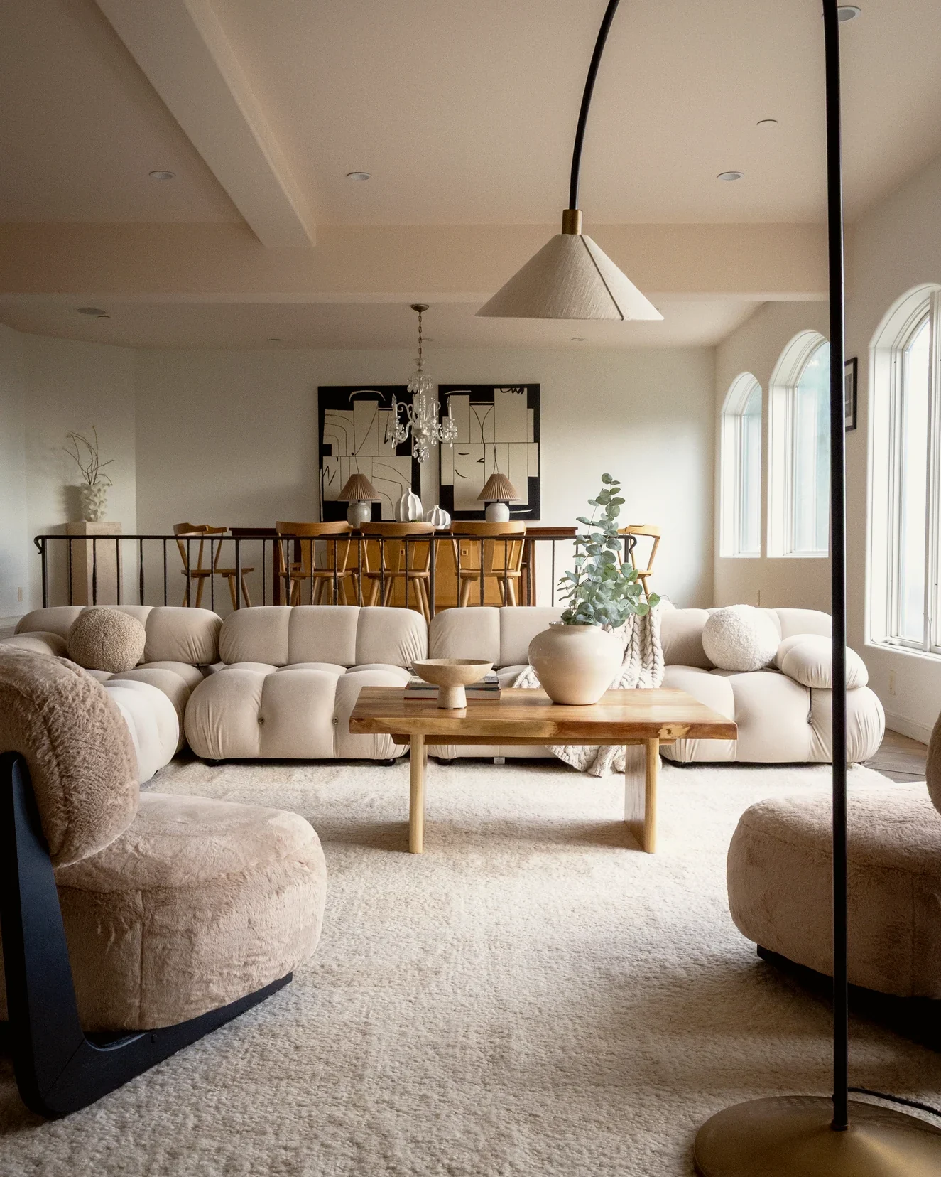Beverly Hills living room with a cream modular sofa, shearling armchairs and a live-edge coffee table, with the spindle-back dining set on the upper level beyond, staged by Nesting Dolls Design