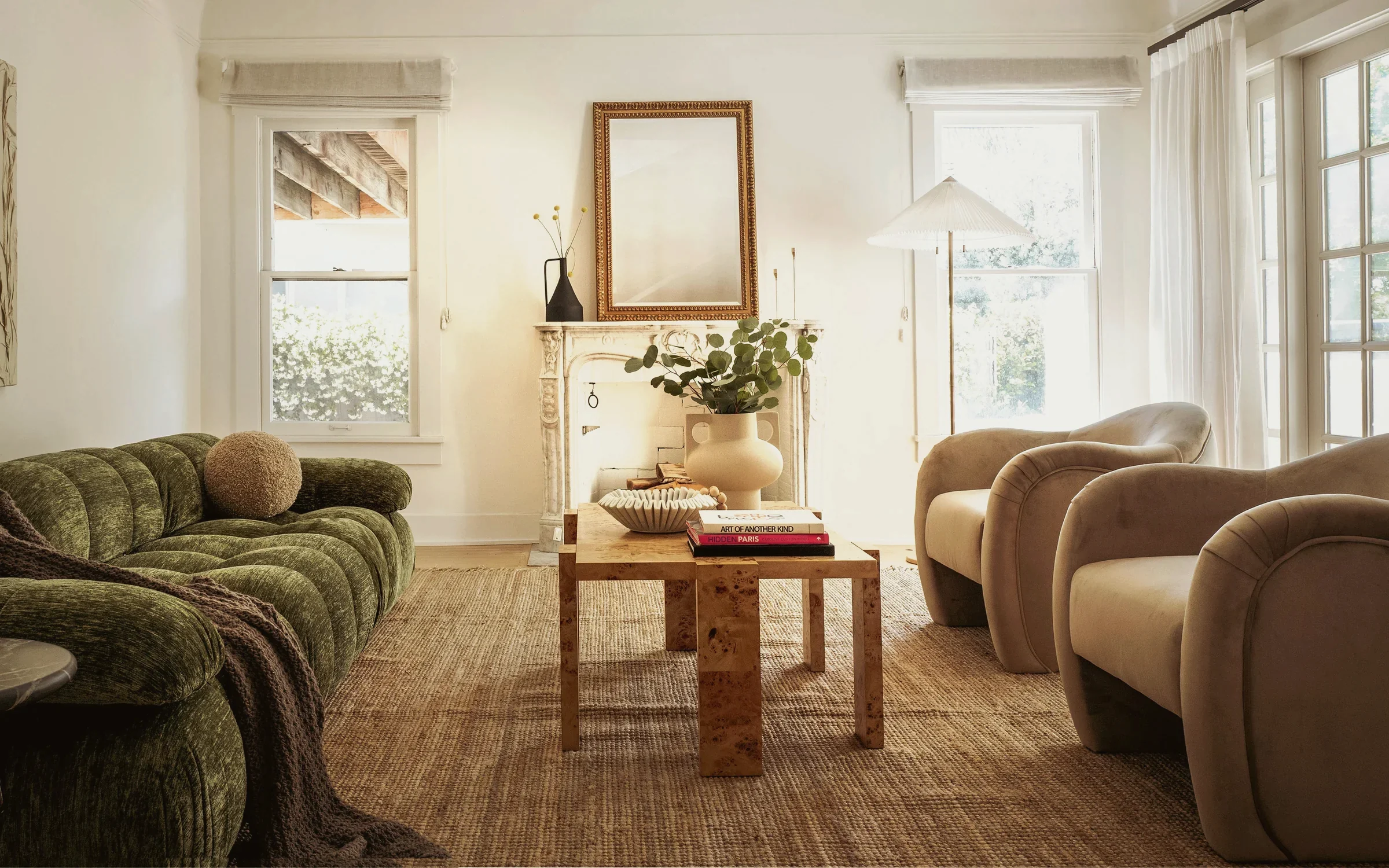 Larchmont 1920s living room with a green chenille sofa, velvet armchairs and an original carved marble mantel, staged by Nesting Dolls Design