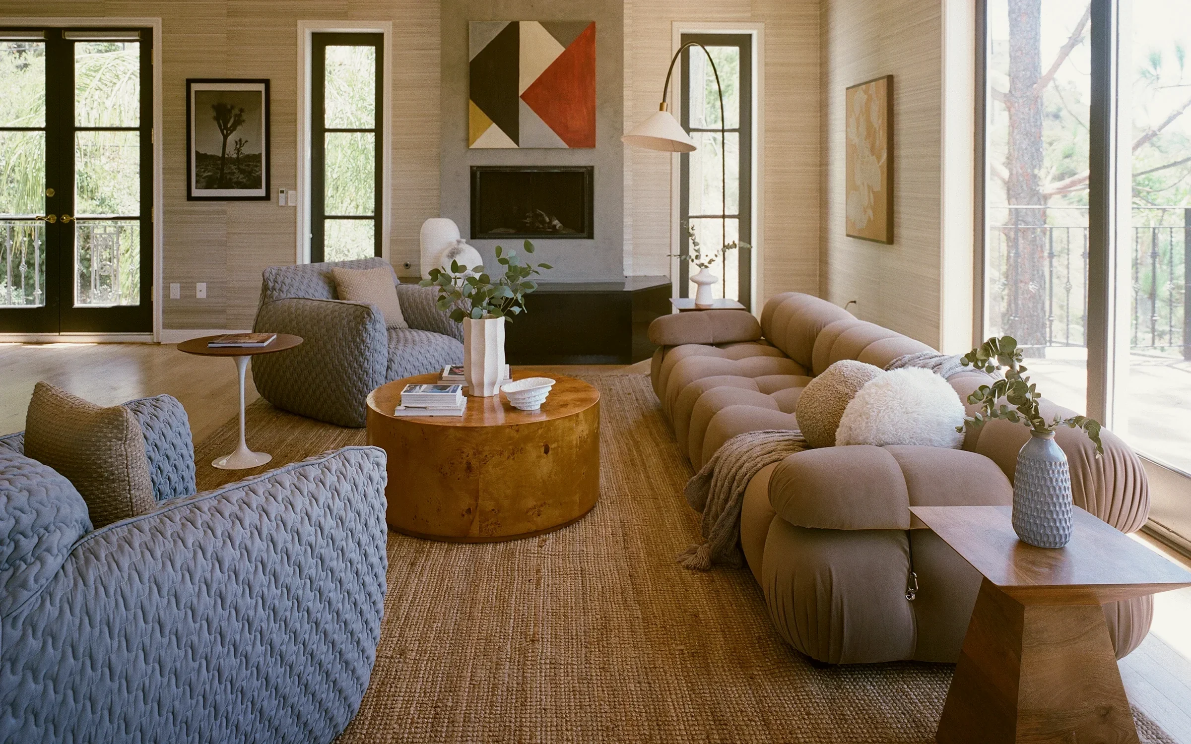 Laurel Canyon living room with quilted blue-gray armchairs, a modular sofa and a geometric canvas above a concrete fireplace, staged by Nesting Dolls Design
