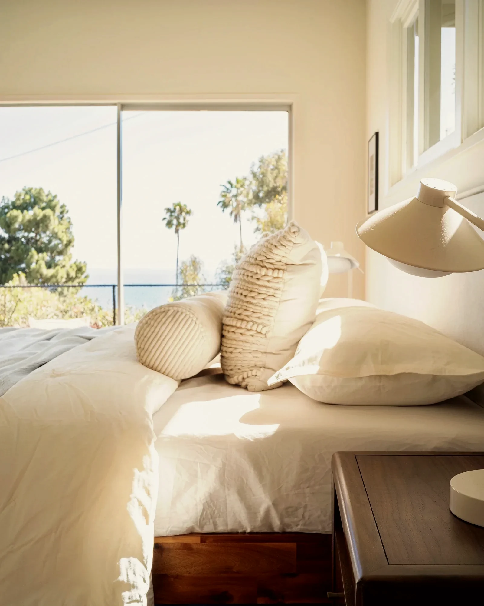 Rancho Palos Verdes bedroom in white linen with textured bolsters and open ocean through the window, staged by Nesting Dolls Design